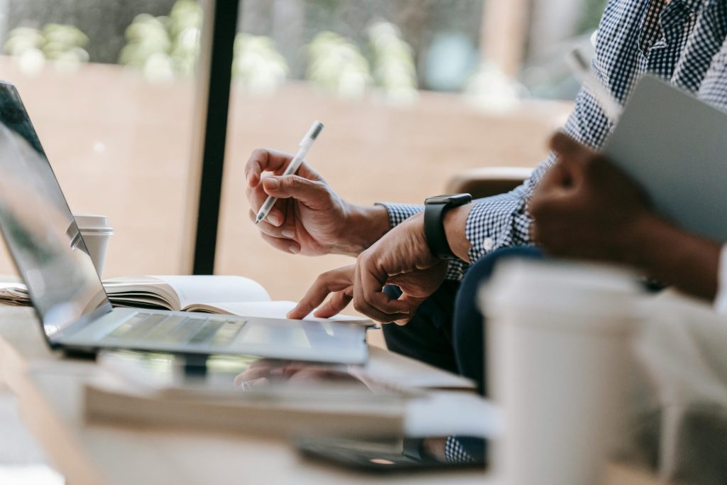 Nahaufnahme von Kollegen, die in einem Bürogebäude an einem Laptop und mit einem Notizbuch an einem Projekt arbeiten.